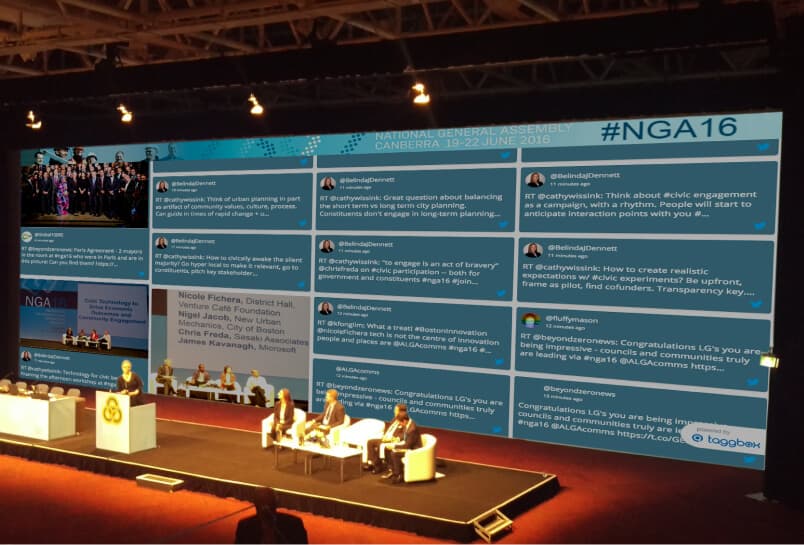 Digital screens at a government event showing campaign updates